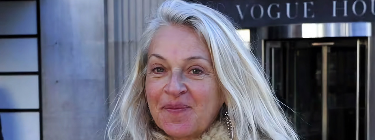 Sue Douglas, British media executive and former newspaper editor, wearing a white coat, pictured outside. In view a partially obscured sign in the background displaying the word Vogue