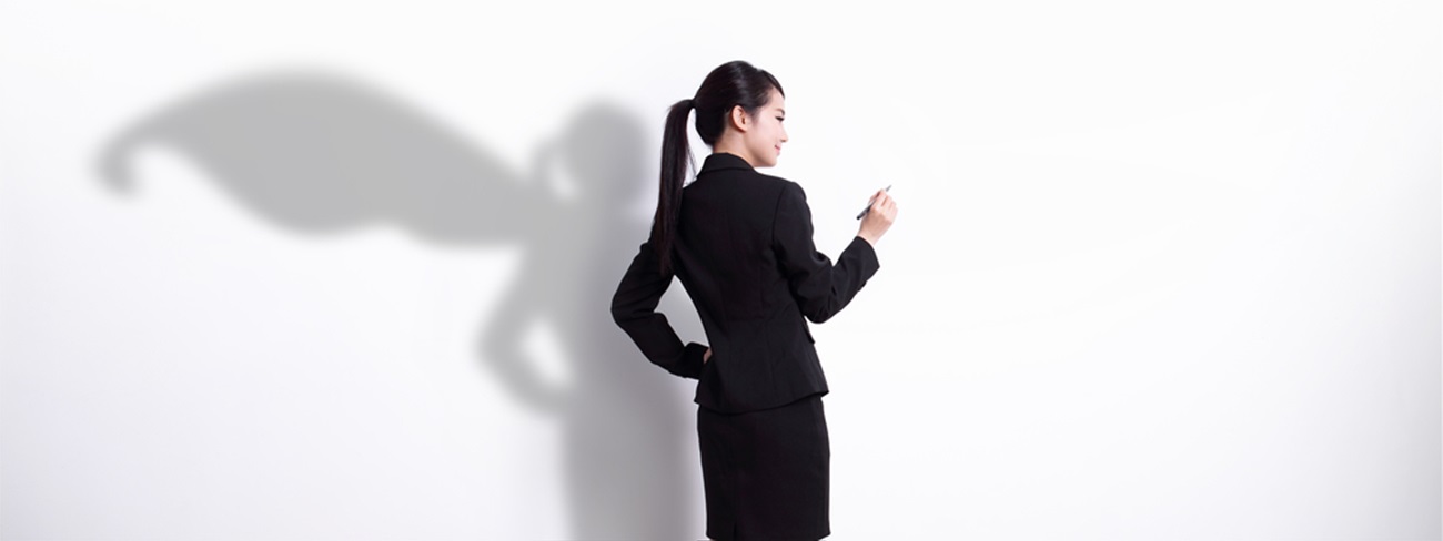 Woman standing against white wall with a shadow wearing a cape